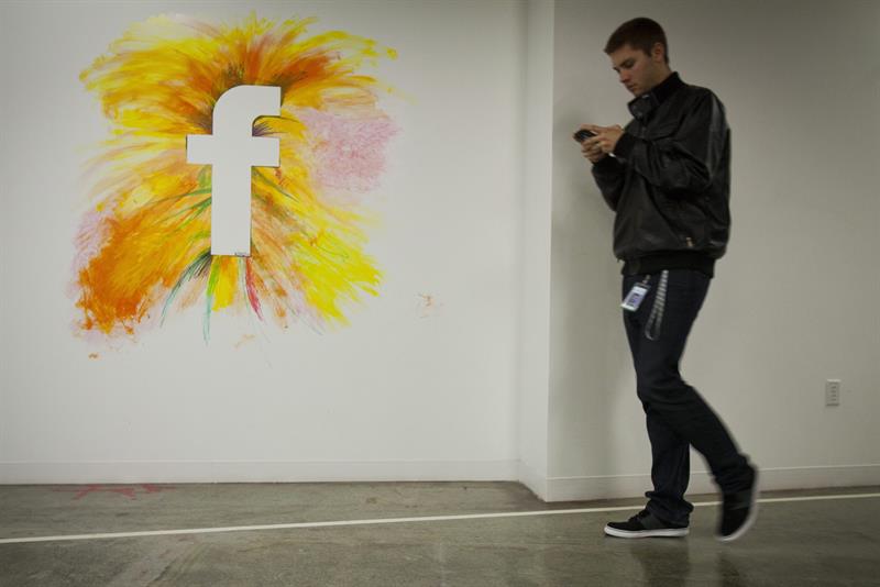 Un empleado camina por un muro con el logo de la red social Facebook. EFE/Archivo