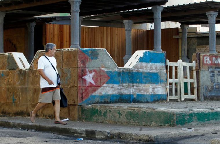 Hombre camina junto a una pintura de la bandera cubana.