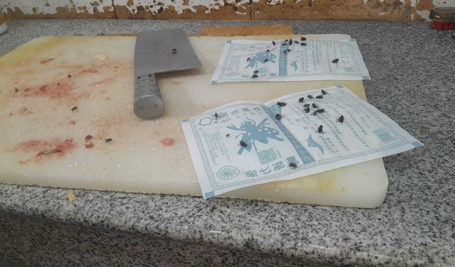 Las moscas merodean tabla de picar y cuchillo para el corte de la carne.