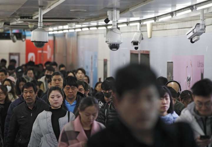 Viajeros caminan junto a las cámaras de vigilancia instaladas en una pasarela entre dos estaciones de metro en Beijing. AP