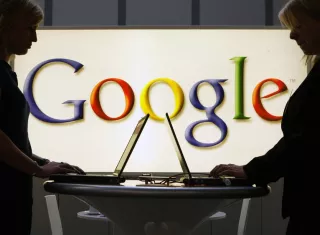 Expositores de Google trabajan frente a un letrero iluminado en la feria industrial Hannover Messe en Hannover, Alemania.  AP