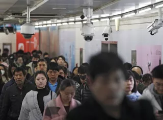 Viajeros caminan junto a las cámaras de vigilancia instaladas en una pasarela entre dos estaciones de metro en Beijing. AP