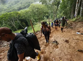 Migrantes suben por una montaña cubierta de lodo. EFE