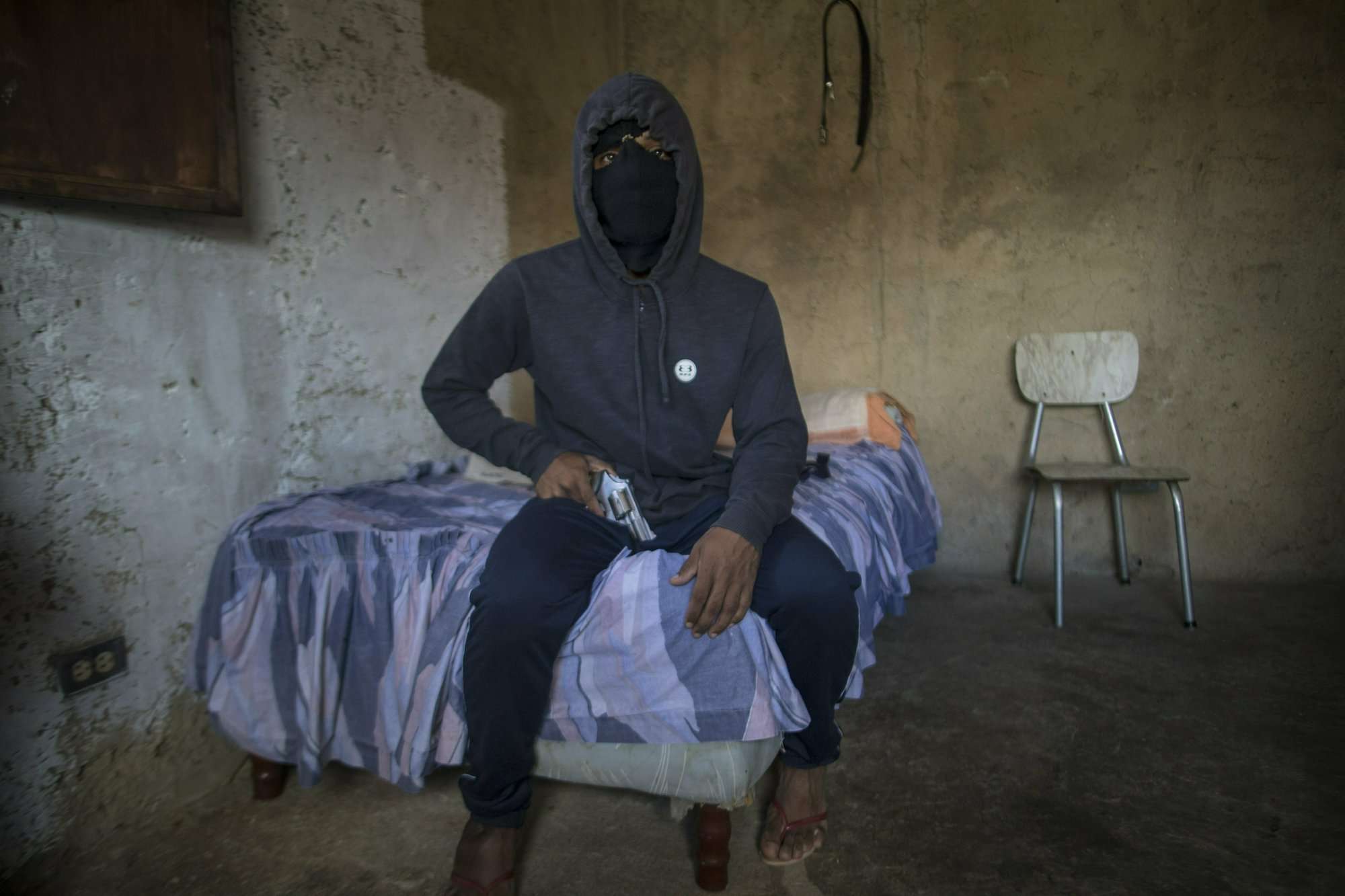 Un gángster enmascarado que recibe el apodo de &quot;El Negrito&quot; posa para un retrato con su arma dentro de la casa de seguridad de su pandilla en el barrio de Petare en Caracas, Venezuela, el lunes 13 de mayo de 2019.  AP