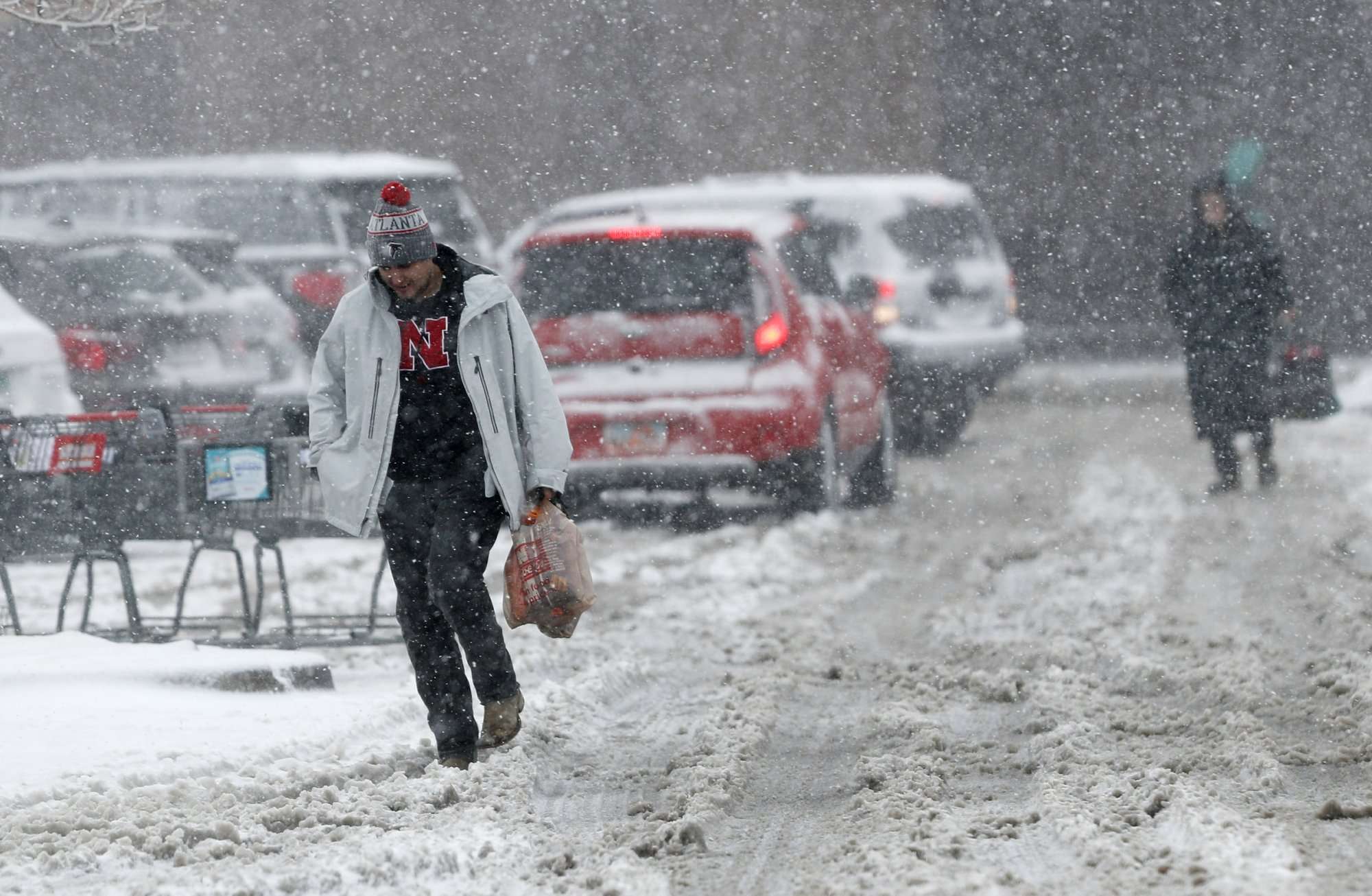 Los compradores luchan para dirigirse a sus vehículos fuera de una tienda de comestibles mientras una tormenta a finales de invierno arrastra vientos huracanados y vientos de nieve en la montaña. AP