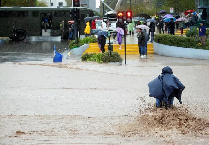 Un hombre en bicicleta intenta cruzar una calle inundada debido a las lluvias en la región metropolitana, donde la autoridad ha decretado "alerta roja".  /  EFE