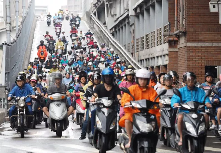 Decenas de motoristas llevan impermeables conduciendo, mientras el Tifón Talim se aproxima, trayendo viento esporádico y lluvias, en Taipei (Taiwán). /  EFE