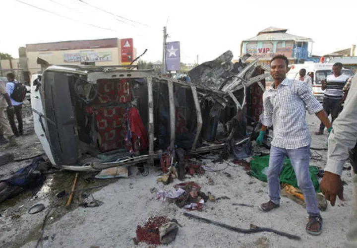 Los somalíes y las fuerzas de seguridad se paran cerca de los restos de un minibús que contiene cadáveres en la escena de un atentado con coche bomba en Mogadiscio, Somalia. /  AP