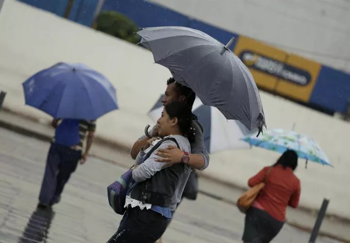 Ciudadanos salvadoreños caminan mientras se protegen de la lluvia en San Salvador. EFE