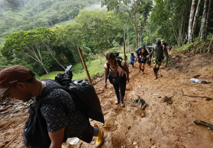 Migrantes suben por una montaña cubierta de lodo. EFE