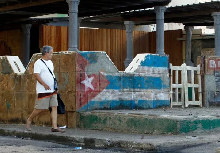 Hombre camina junto a una pintura de la bandera cubana.